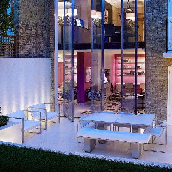 Image of London townhouse back terrace at nighttime, with FueraDentro minimalist garden dining furniture and lounge chairs