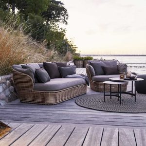 Image of Cane-line Basket garden sofa in natural Cane-line weave with taupe cushions, with grasses and grey sea and sky in background