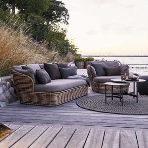 Image of Cane-line Basket garden sofa in natural Cane-line weave with taupe cushions, with grasses and grey sea and sky in background