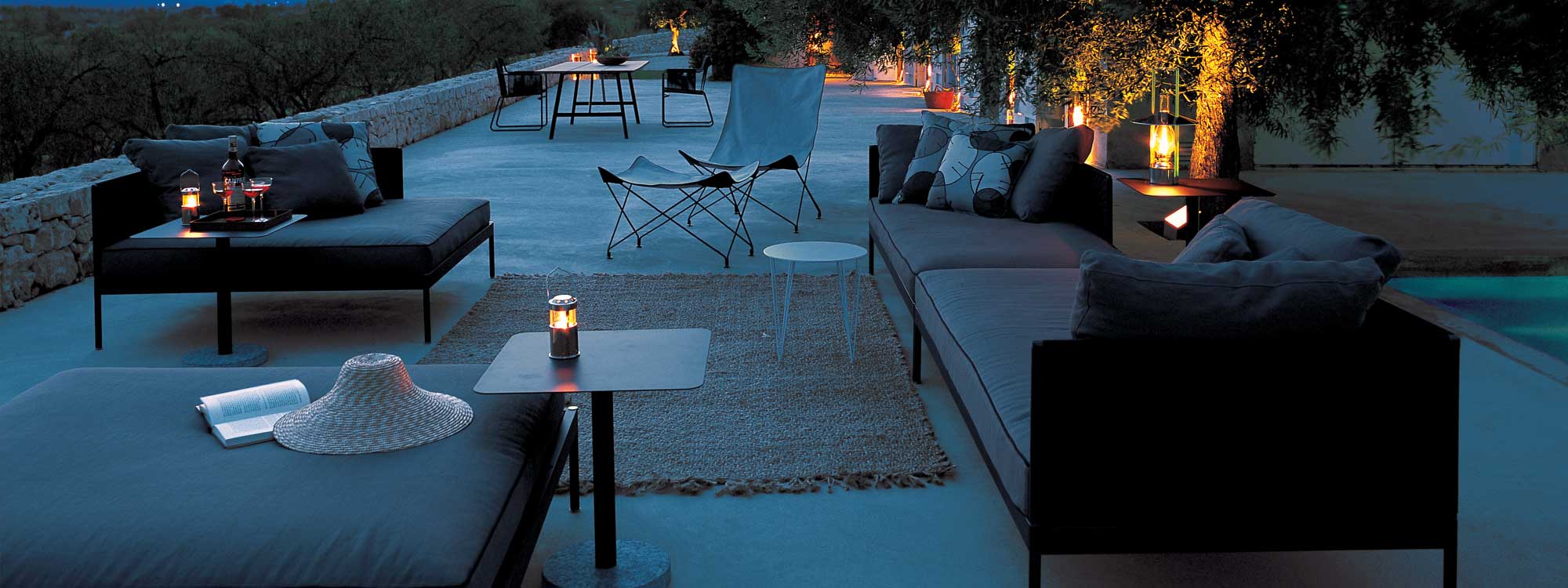Image of RODA Basket outdoor sofa and daybed on terrace at dusk, with Lawrence butterfly chair and Harp dining chairs in background