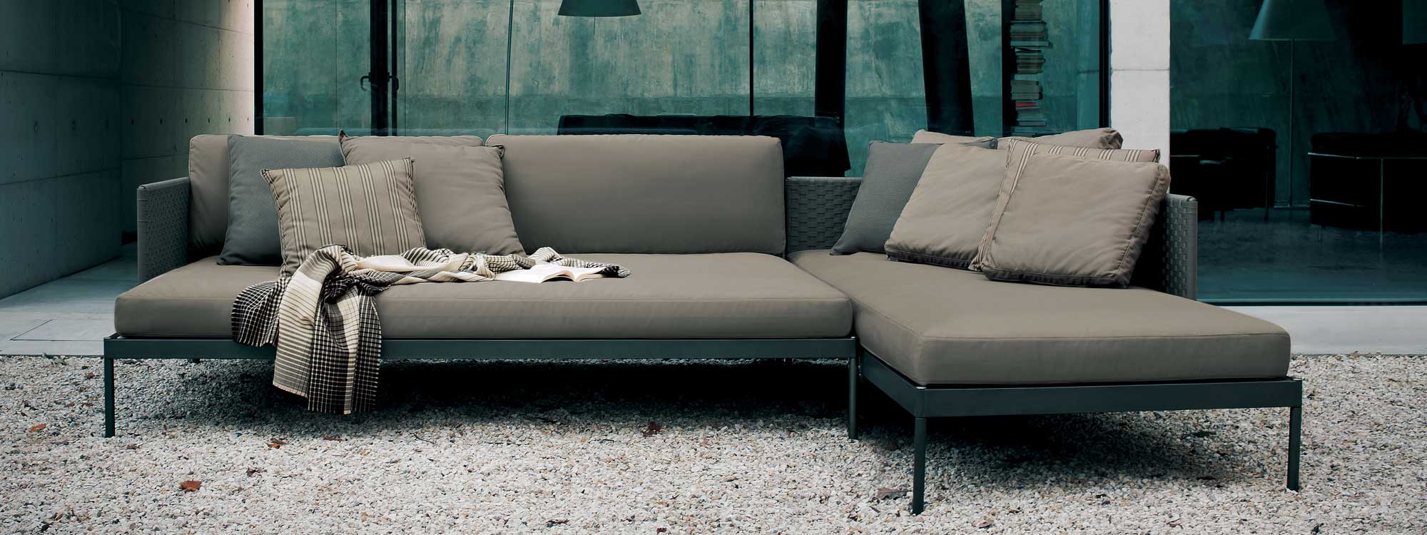 Image of Basket outdoor corner sofa with smoke colored aluminum frame and taupe cushions, shown on gravel courtyard