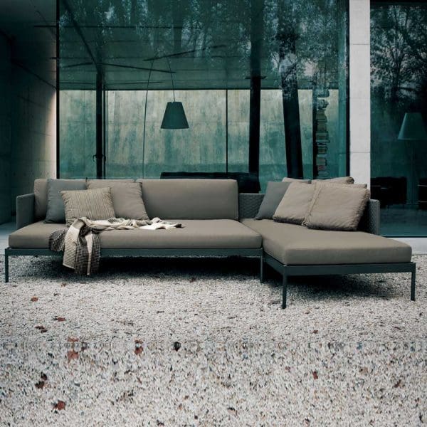 Image of RODA Basket small garden corner sofa on gravel, with floor to ceiling glass window in background