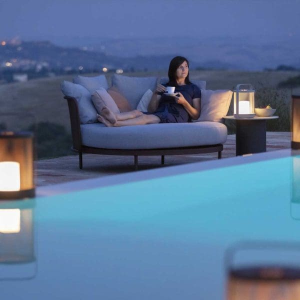 Image of woman drinking a coffee whilst lying on Baza outdoor daybed on poolside in fading light