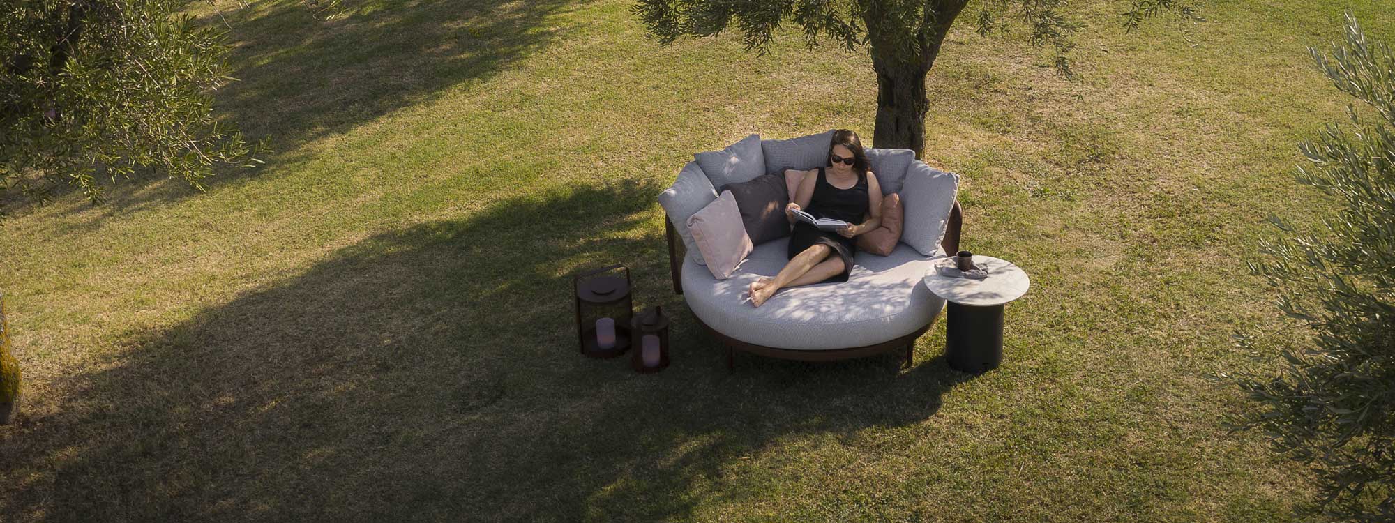 Image of woman relaxing on Baza luxury garden daybed beneath shade of tree