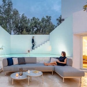 Image at dusk of Todus modern outdoor corner sofa and Starling round low tables with illuminated plunge pool and whitewashed walls in the background