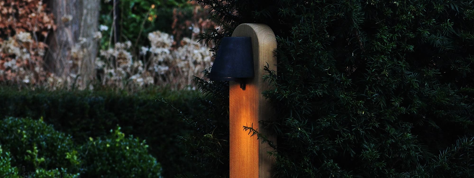 Nighttime image of Royal Botania Beamy teak post light surrounded by Taxus baccata