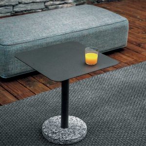 Image of smoke coloured Bernardo coffee table with square HPL top and circular stone base, with glass of orange juice on table top