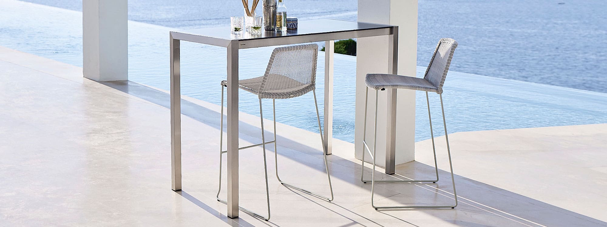 Image of white-grey Breeze modern outdoor bar stools and Cane-line bar table on poolside