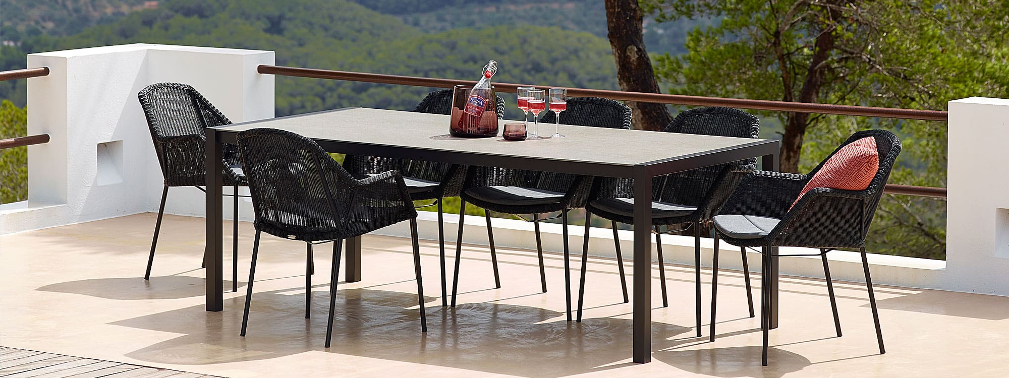 Image of black Cane-line Breeze stacking garden chairs around a dining table with 3 glasses of rose wine and wine bottle on table top