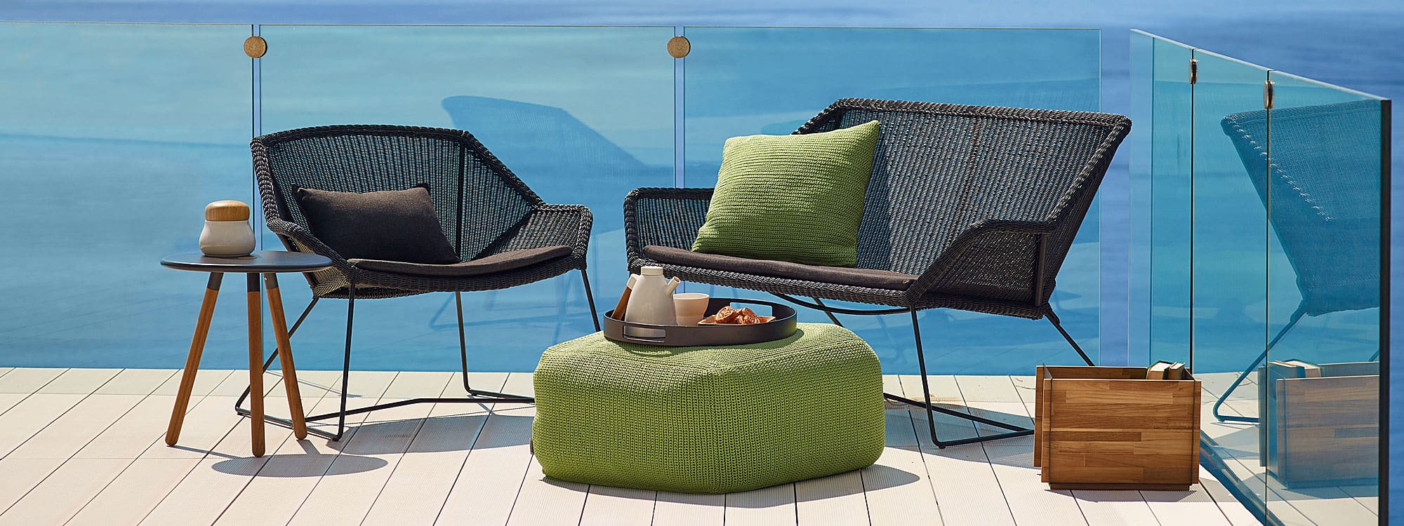 Image of black Breeze 2 seat garden sofa and woven outdoor easy chair in Cane-line weave, together with Divine outdoor pouf and Area round side table