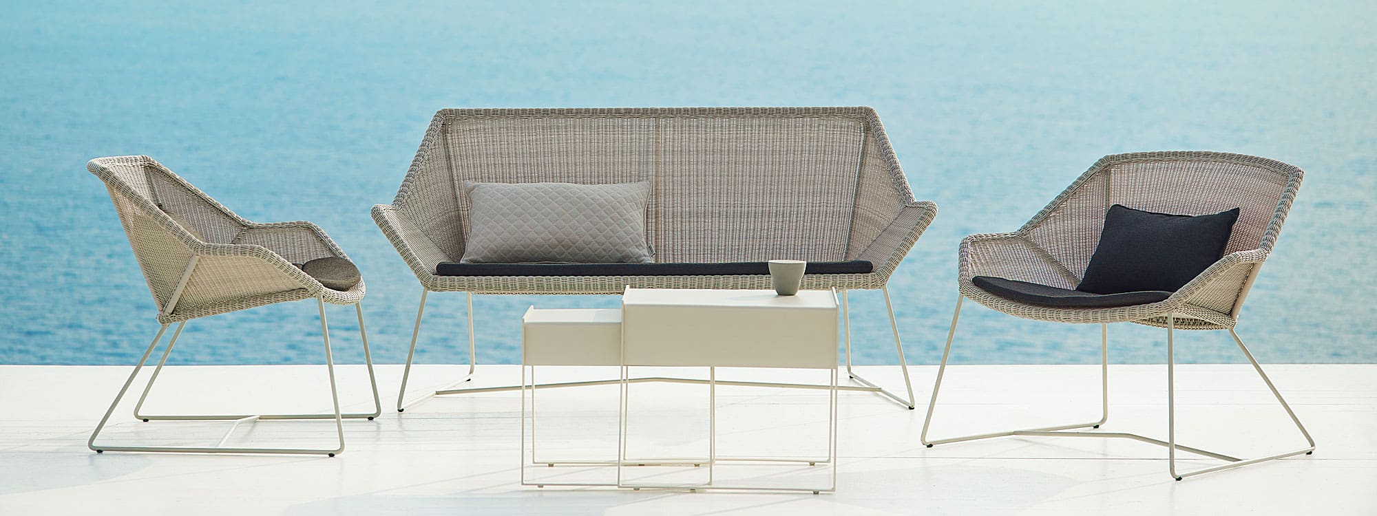 Image of white-grey Breeze 2 seat garden sofa and outdoor rattan lounge chairs by Cane-line, with sea in background
