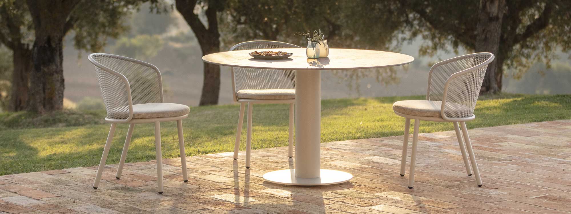 Image of white Branta circular outdoor table and Baza garden chair in warm evening sunlight