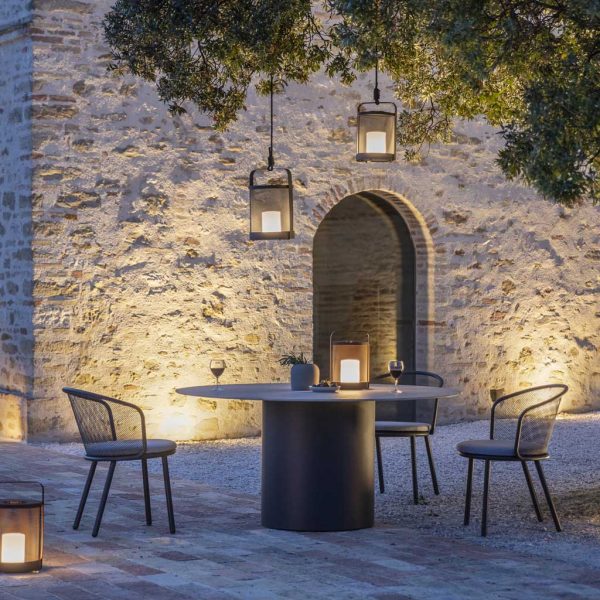 Image of Todus Branta modern outdoor dining table and Baza chairs on illuminated courtyard beneath large tree