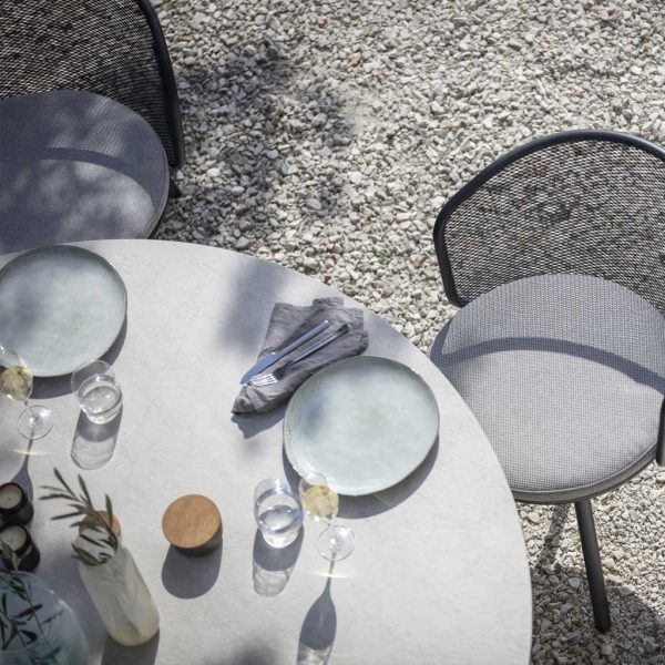 Image of aerial view of Branta circular garden table's ceramic table top, set ready for dinner, with Baza garden chairs to the side