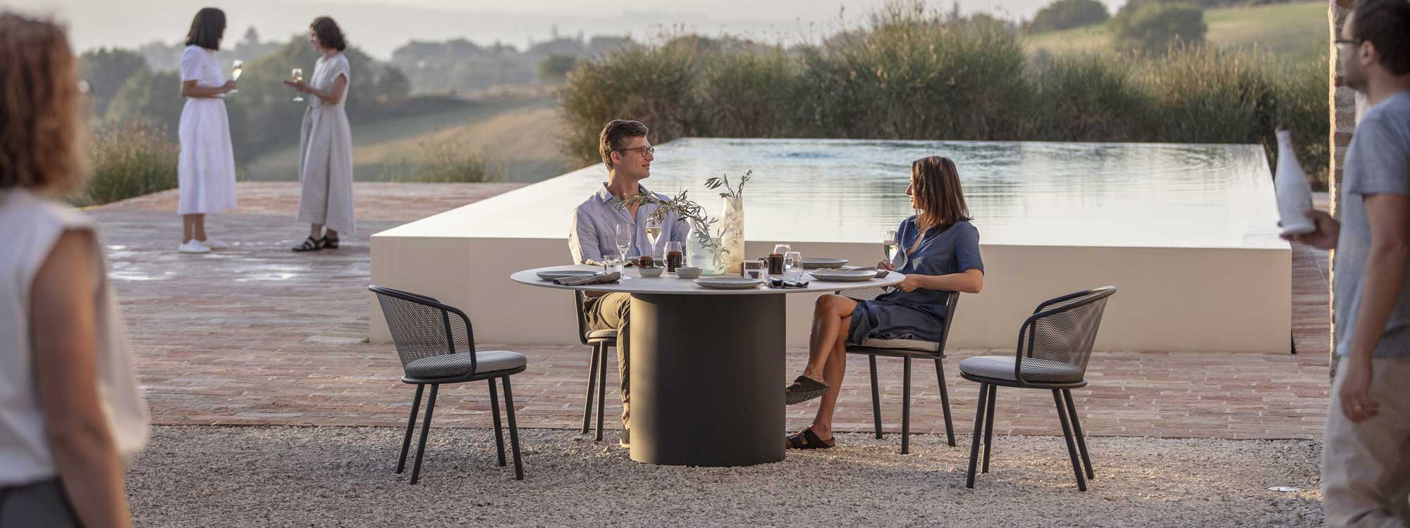 Image of Branta large round garden table and Baza outdoor dining chairs on terrace in front of swimming pool and olive trees