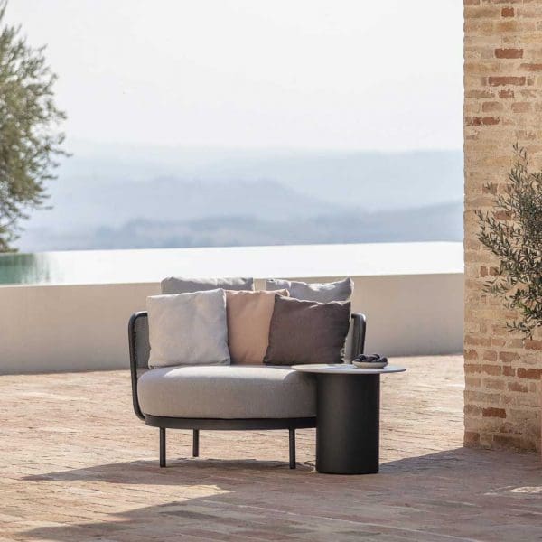 Image of Todus Branta round garden side table with Baza outdoor lounge chair on terrace with horizon swimming pool and hazy hills in the background
