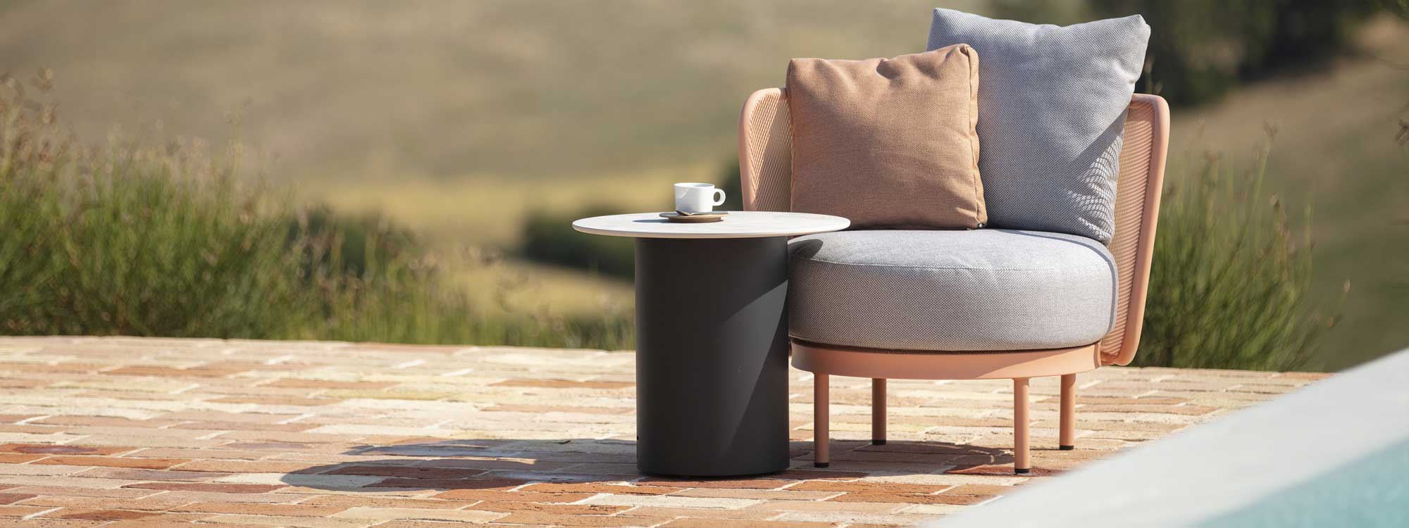 Image of salmon pink-colored Baza Club garden lounge chair and Branta anthracite side table with white top on sunny terrace