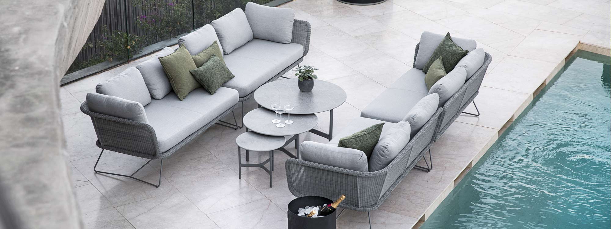 Image of pair of Caneline Horizon garden sofas in grey weave and grey cushions, with nest of round Twist tables in the middle