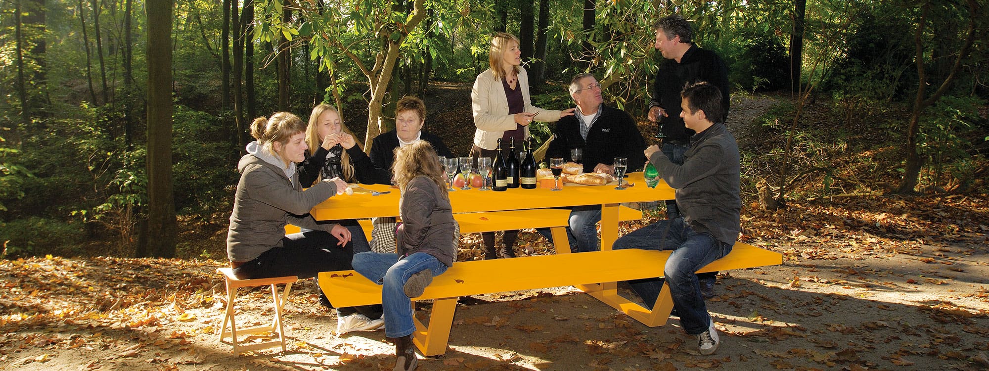 Image of family and friends sat around Cassecroute yellow modern picnic table with woodland in the background