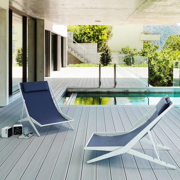Image of pair of Boomy luxury deck chairs with white frames and blue slings, shown in wooden decked terrace beside swimming pool.