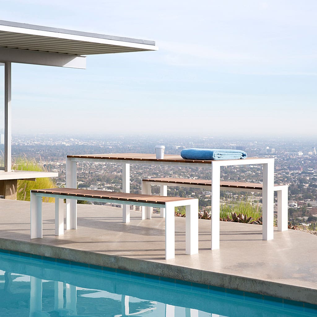 Image of Stua Deneb large garden table and benches with white aluminium frames and slatted teak surfaces, with smoggy cityscape in the background
