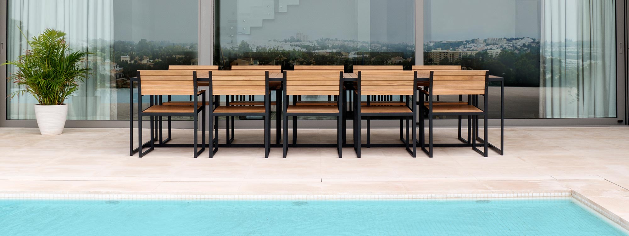 Image of Roshults Garden Bistro large dining table and chairs on poolside, with floor to ceiling sliding glass doors in the background