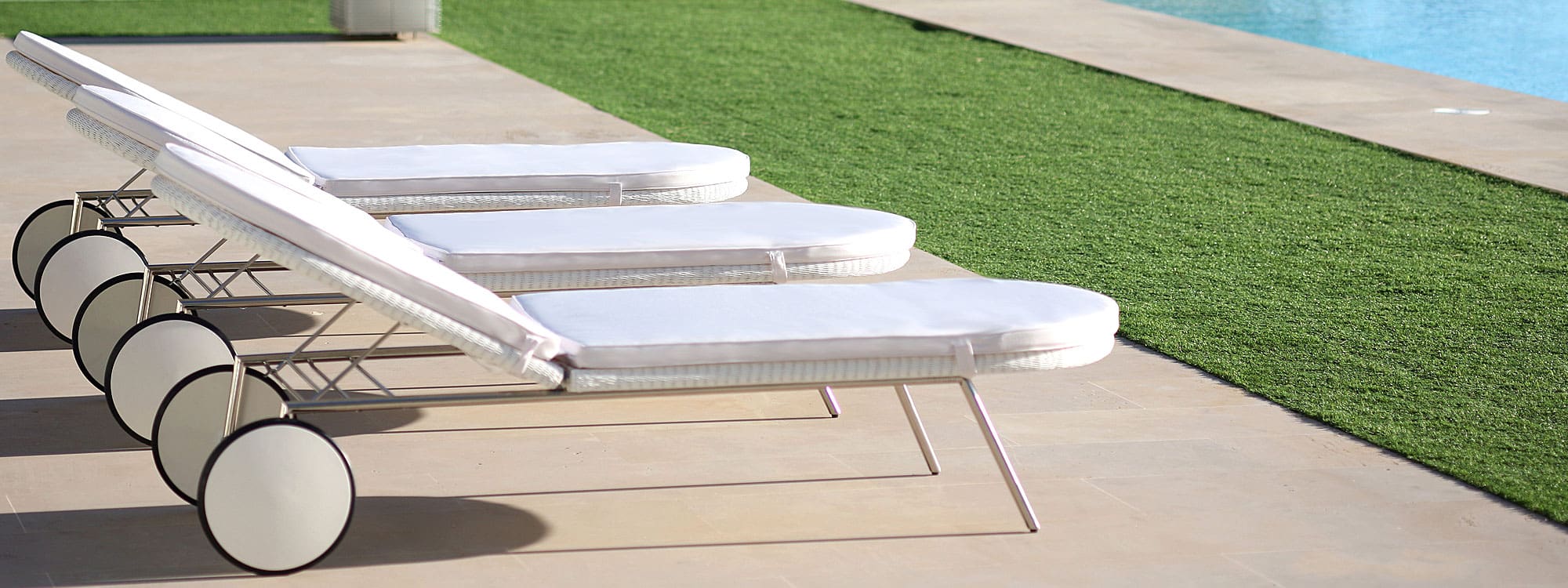 Image of row of 3 white Shell retro-inspired sun loungers on sunny poolside