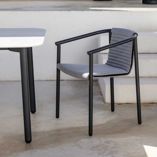Image of Duct Round garden chair in anthracite colored tubular stainless steel and upholstered back and seat, shown next to Starling ceramic garden table in shady courtyard