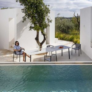 Image of woman sat on Duct Round modern garden armchair next to Starling contemporary outdoor table in whitewashed courtyard, with plunge pool in foreground