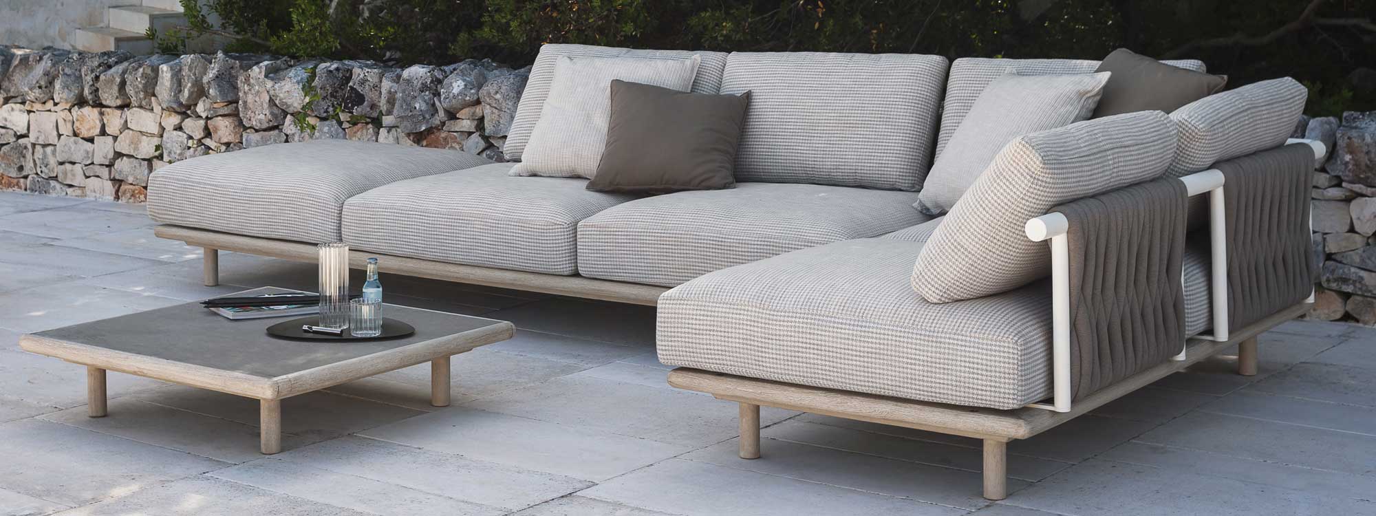 Image of RODA Eden outdoor corner sofa with white-washed teak base and luxury cushions, with low table with farsena natural stone table top