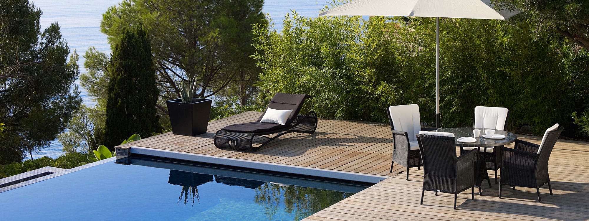 Image of Cane-line's Escape adjustable black sun lounger on wooden decking next to sunny poolside