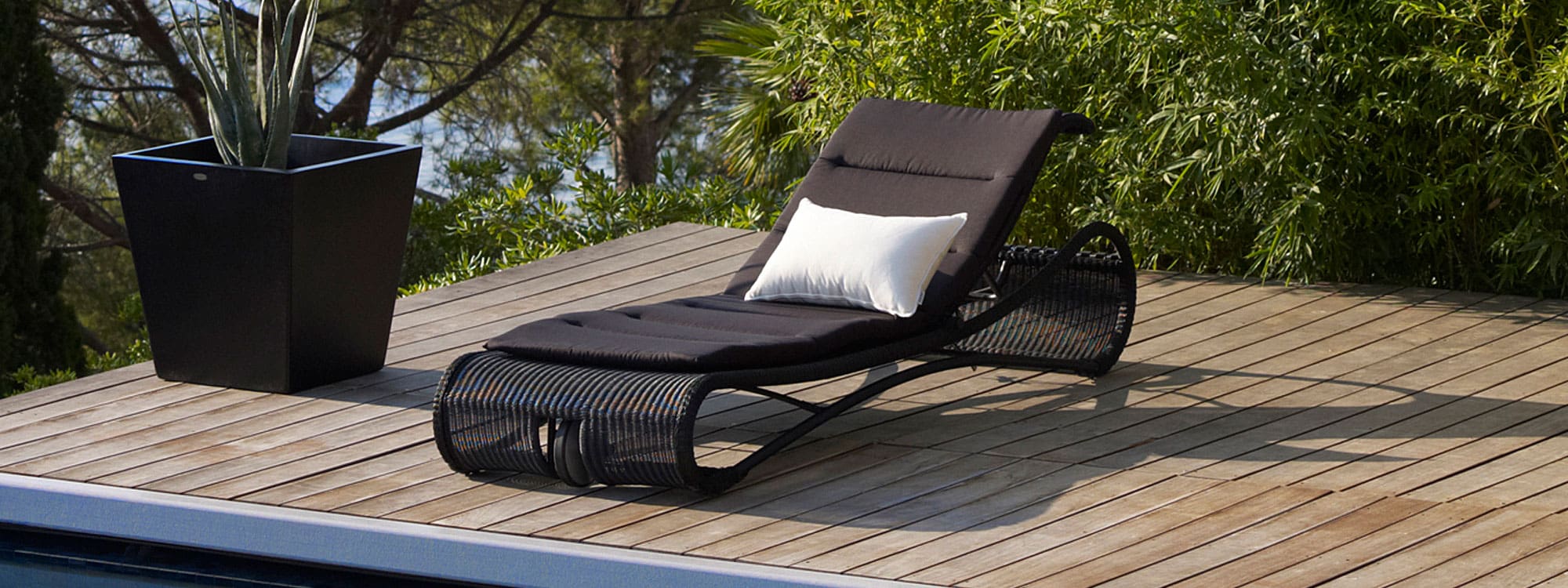 Image of Escape modern sun lounger in black Cane-line weave on wooden decking next to swimming pool