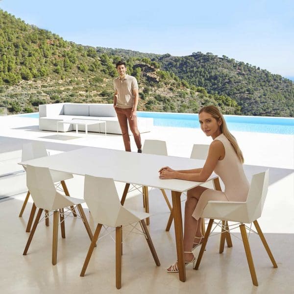 Image of woman sat at Vondom Faz Wood modern dining set with swimming pool and hillside in the background