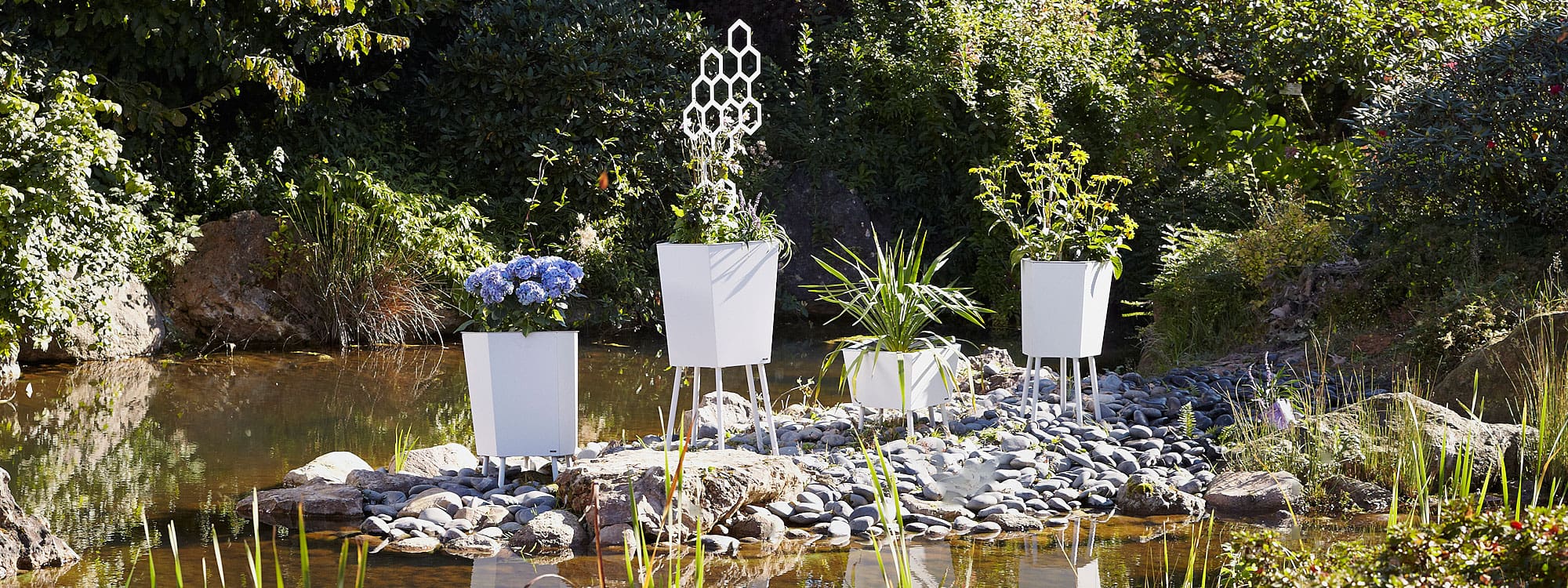 Image of different sizes of Elevation white modern plant pots by Flora, shown on stony shore