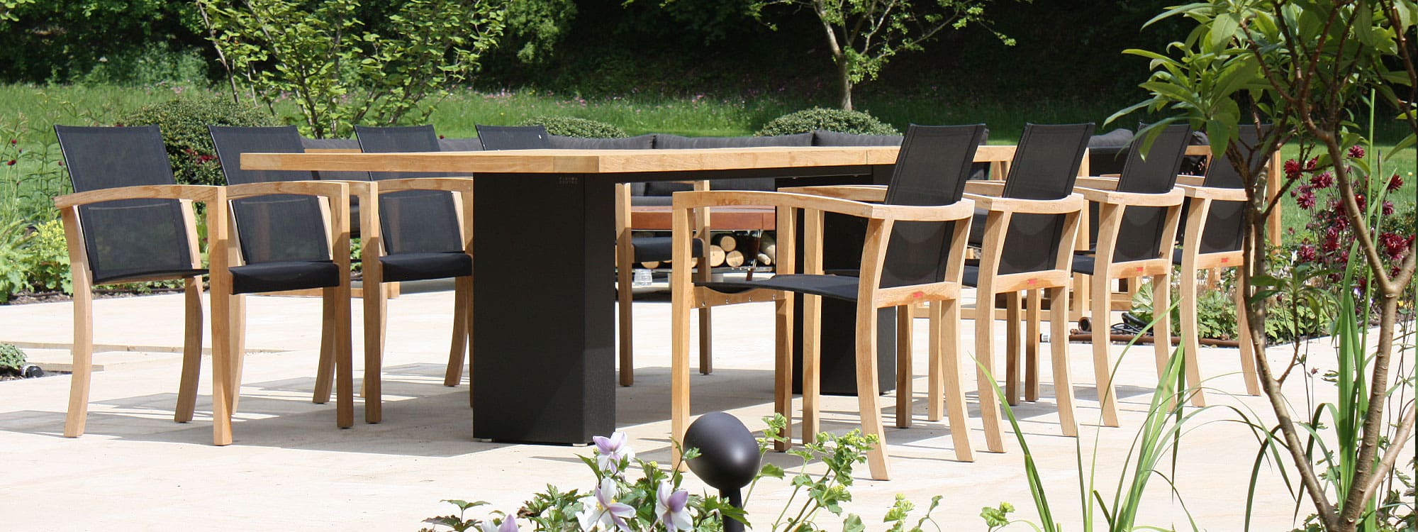 Image of Doble architectural garden table with black pedestal legs and teak top, together with XQI teak and Batyline garden chairs