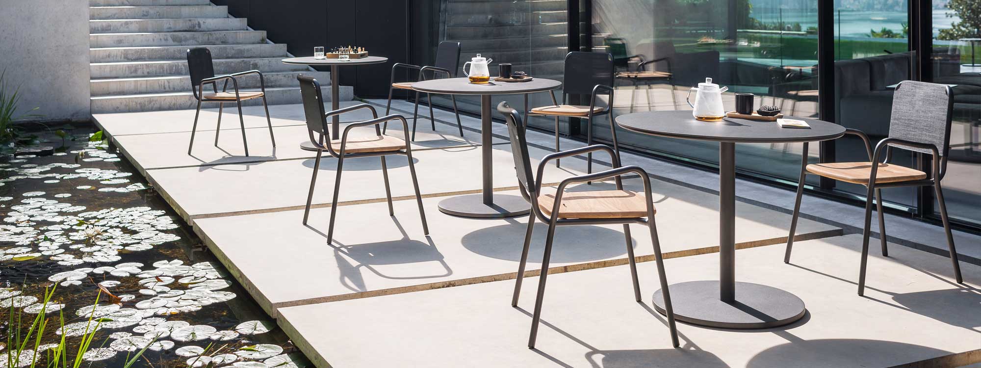 Image of 3 Stem bistro tables and Guest modern dining chairs by RODA on terrace next to calm water feature with water lillies