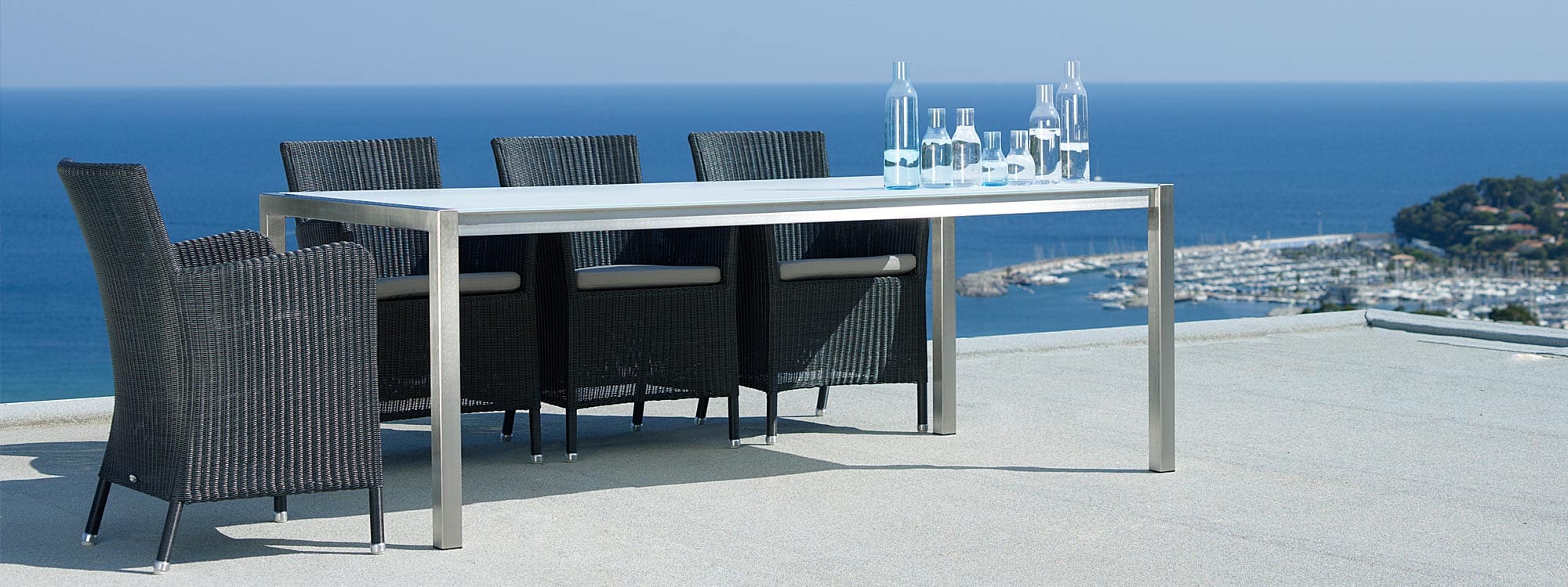 Image of Hampsted black whicker garden chairs on sunny terrace around Caneline dining table with port and sea in background