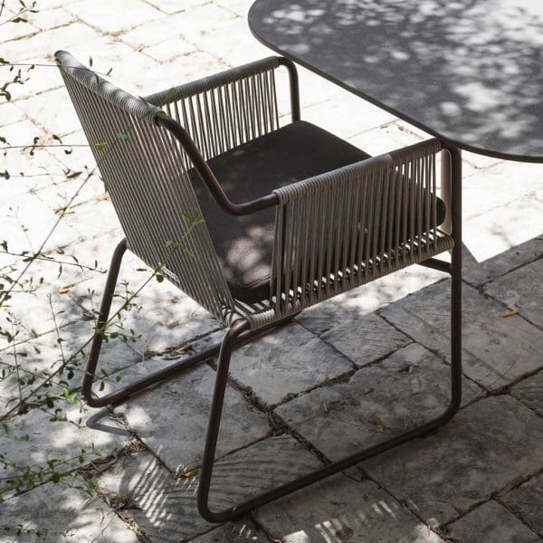 Image of RODA Harp garden chair with smoke colored frame and olive colored acrylic weave, net to Piper extending garden table