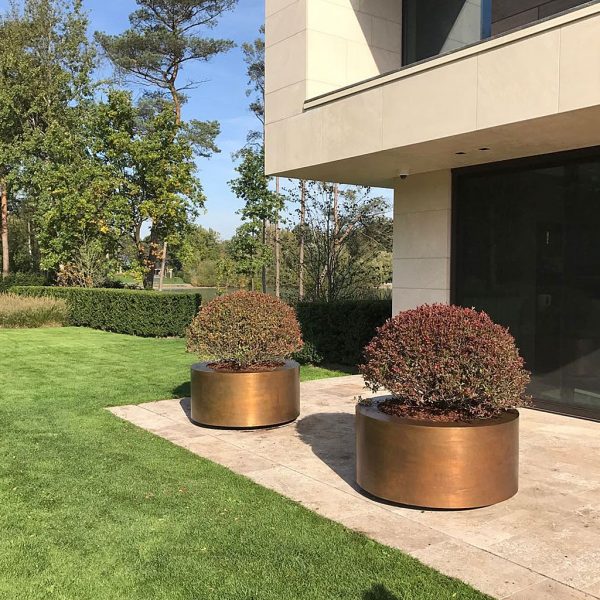 Image of pair of polished brass circular planters by Cuprum on terrace outside modernist house