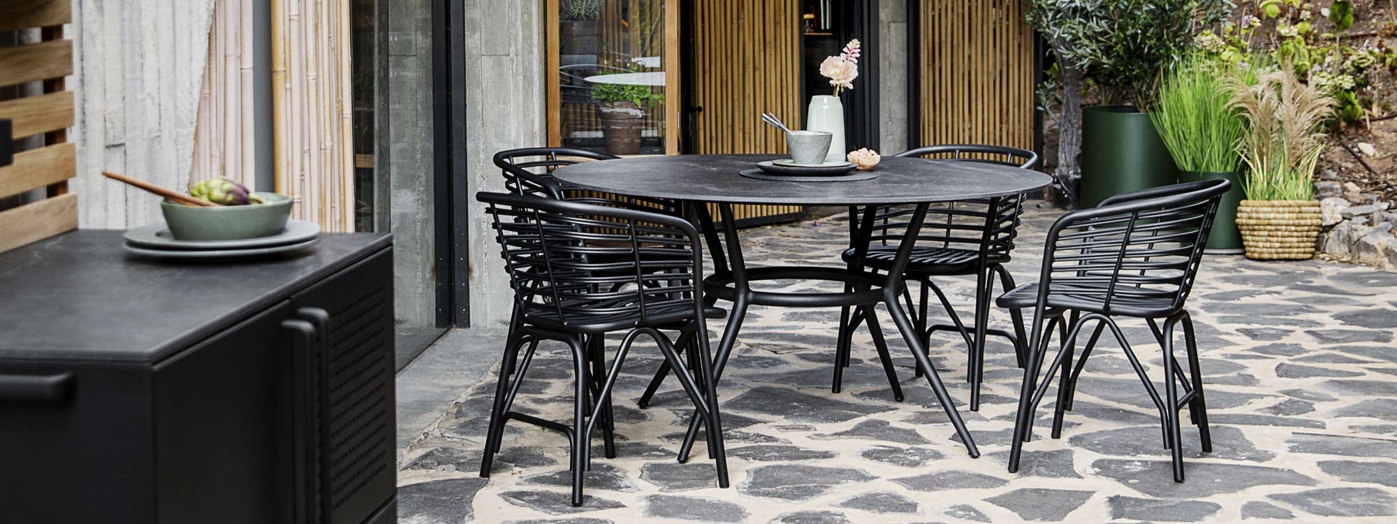 Image of Joy circular garden table with black Fossil ceramic top, together with Lava-grey blend chairs by Cane-line