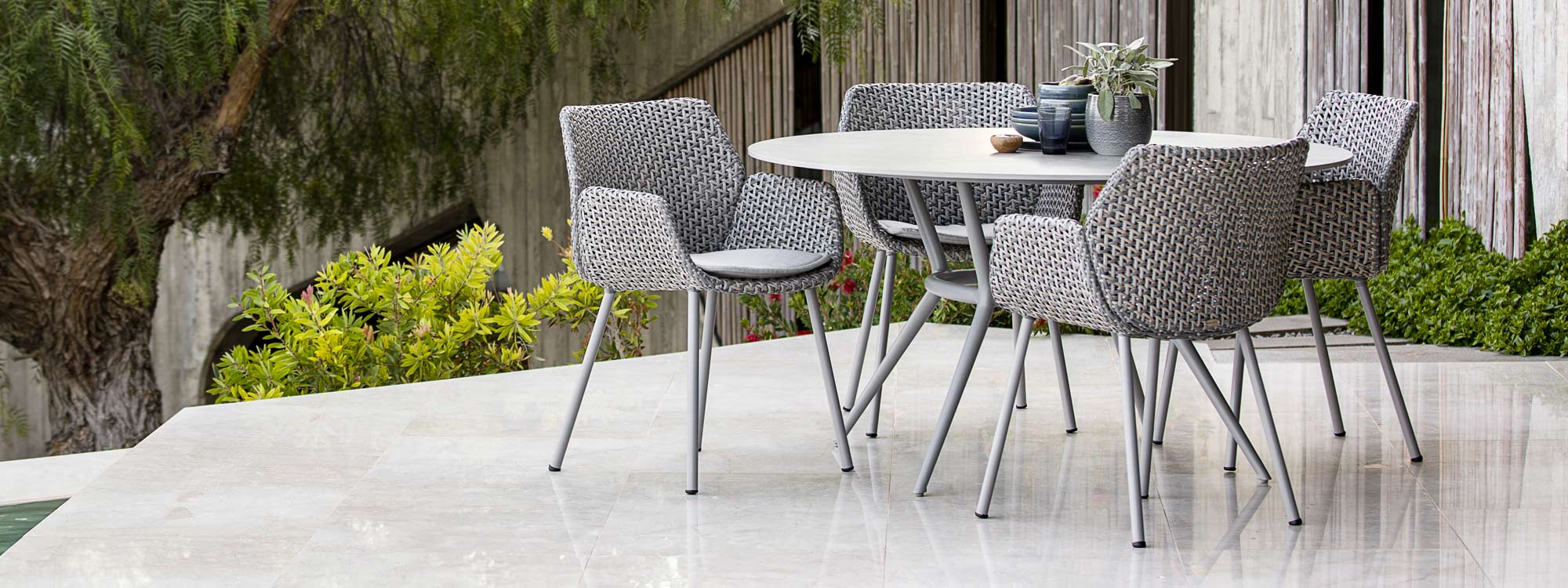 Image of Joy circular dining table and Vibe rattan garden armchairs by Cane-line, shown in sleek outdoor terrace