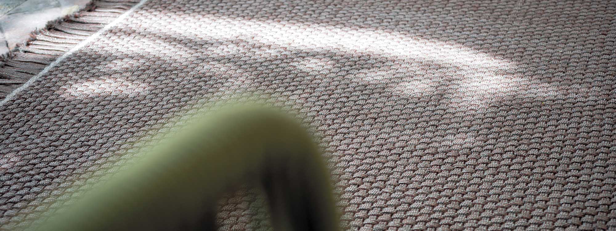 Image of detail of RODA Knot luxury outdoor carpet, with tubular arm of Harp garden chair in foreground