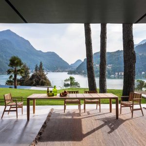 Image of RODA Levante modern teak dining set on terrace beneath cantilevered ceiling with trees, lake and hills in background