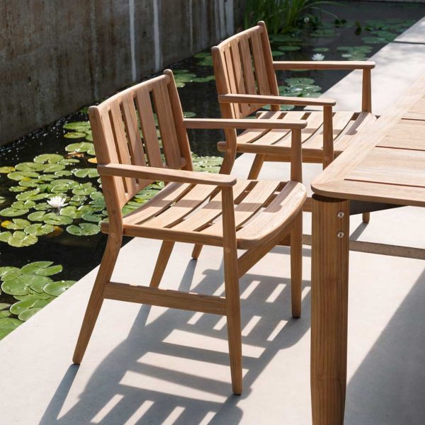 Image of pair of Levante teak garden chairs and outdoor dining table by RODA on sunny terrace, with tranquil water feature in background with lily pads