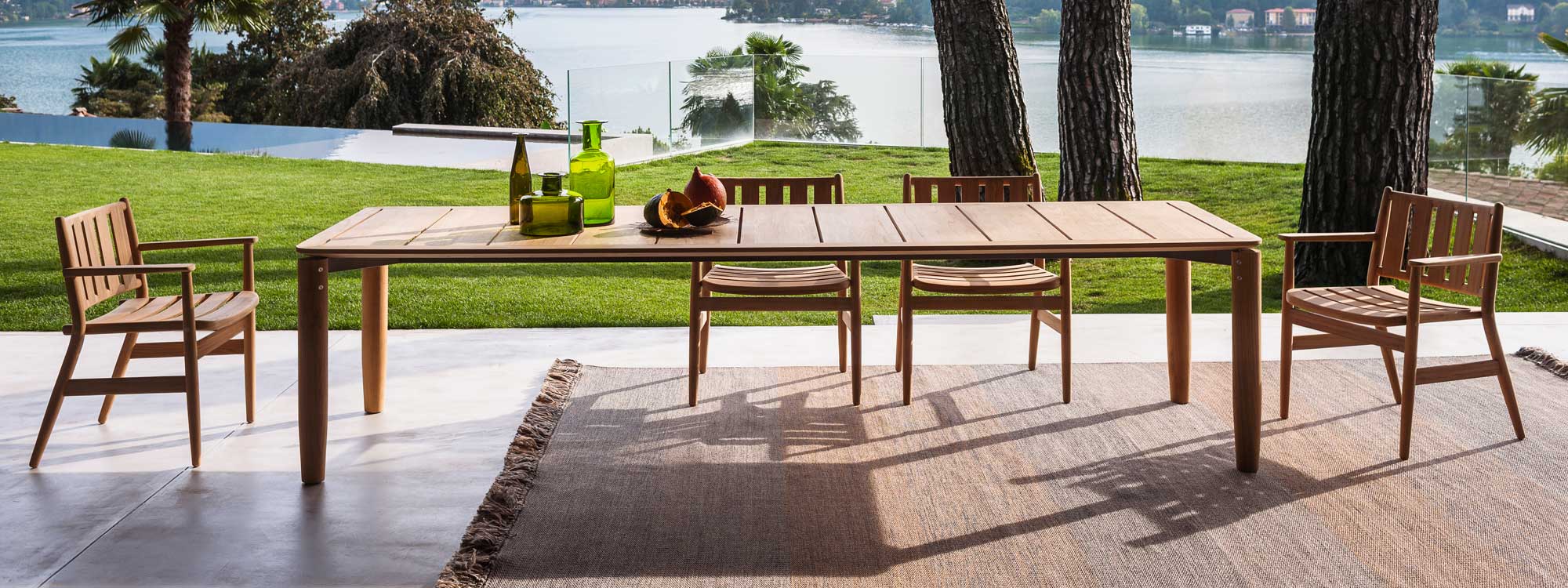 Image of large Levante teak dining table and chairs by Piero Lissono for RODA, shown on terrace with trees, lake and hills in background
