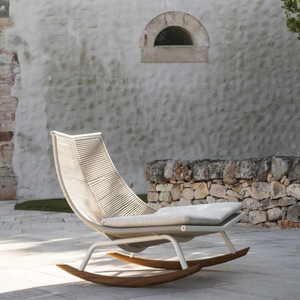 Image of RODA Laze minimalist garden rocking chair with white frame and teak skids, shown in light and shade of rustic Italian courtyard