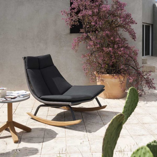 Image of RODA Laze black rocking chair with teak skids, with cactus in foreground of terrace