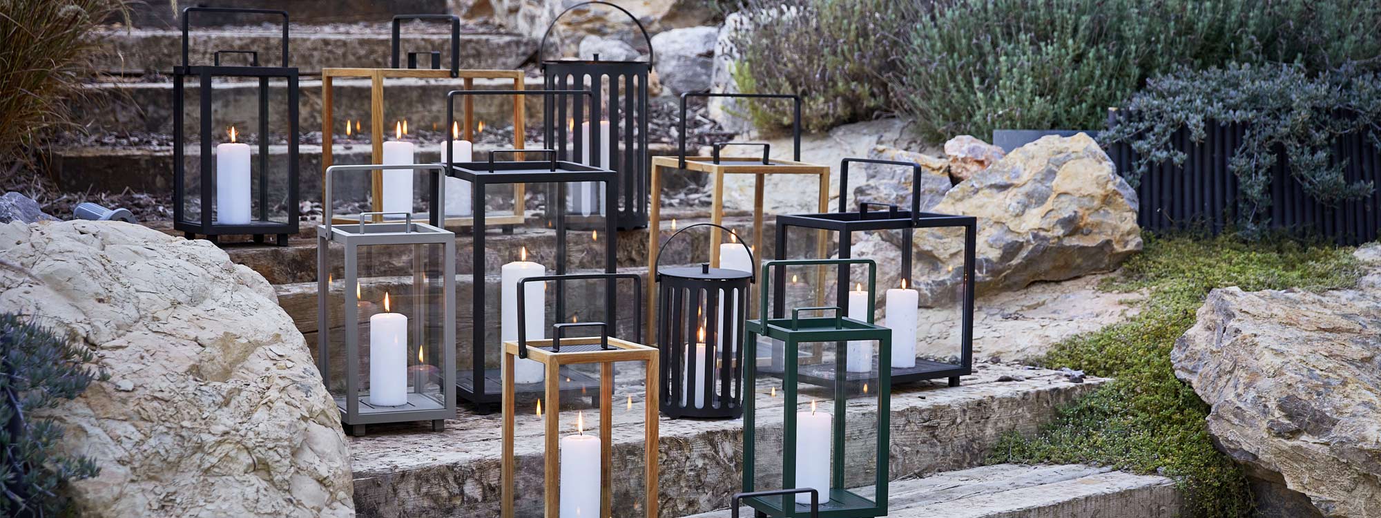 Image of many different sizes and colour finishes of Lighthouse lanterns by Cane-line, with candles burning inside