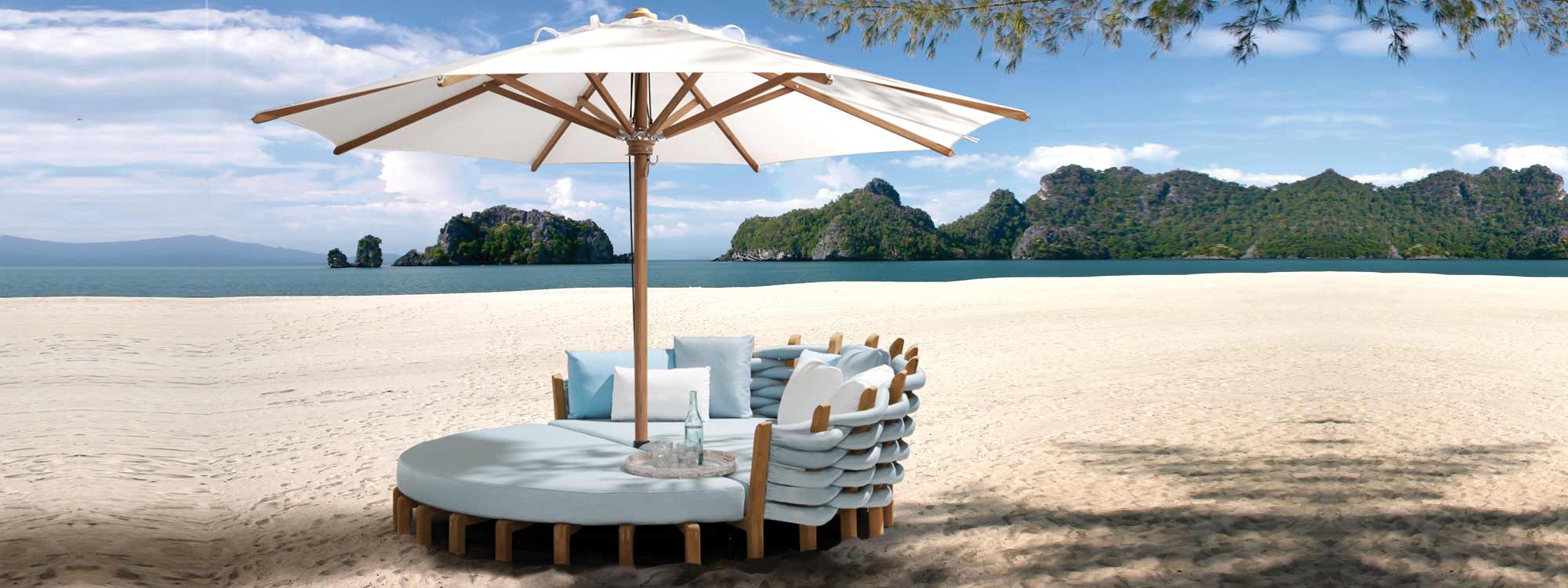 Image of Royal Botania Lotus modern garden day bed with sky blue cushions and white Shady Teak parasol on sandy beach.