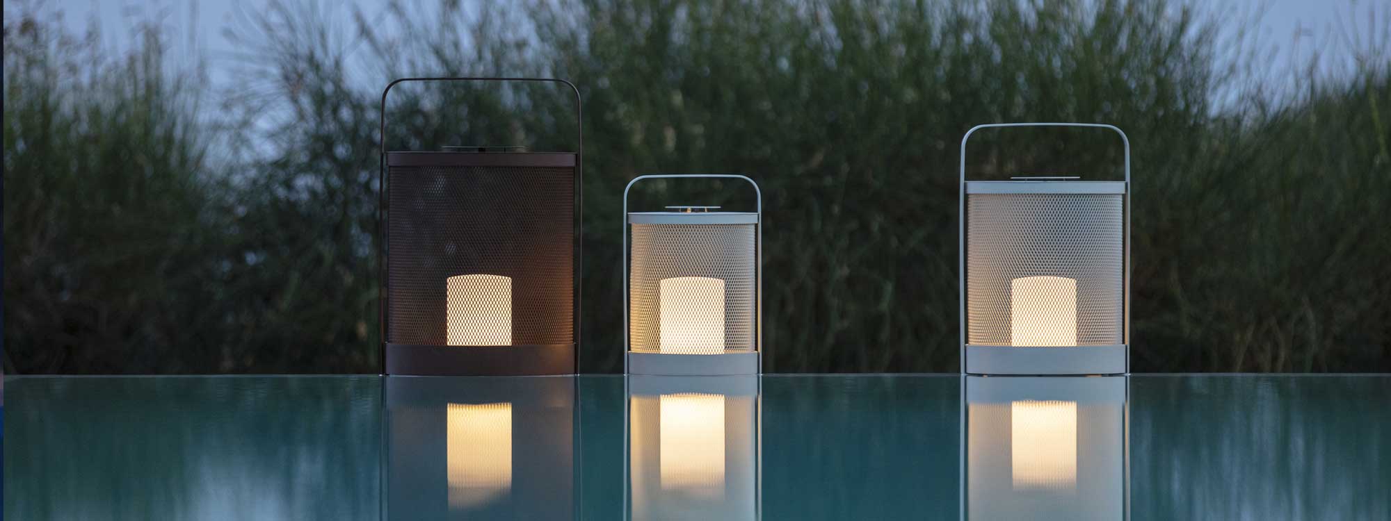 Image of 3 sizes of Luci modern garden lanterns reflected in water of swimming pool